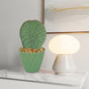 Beavertail Cactus (Opuntia basilaris) in a green pot on a white tabletop next to a round lamp, with abstract art on the wall.