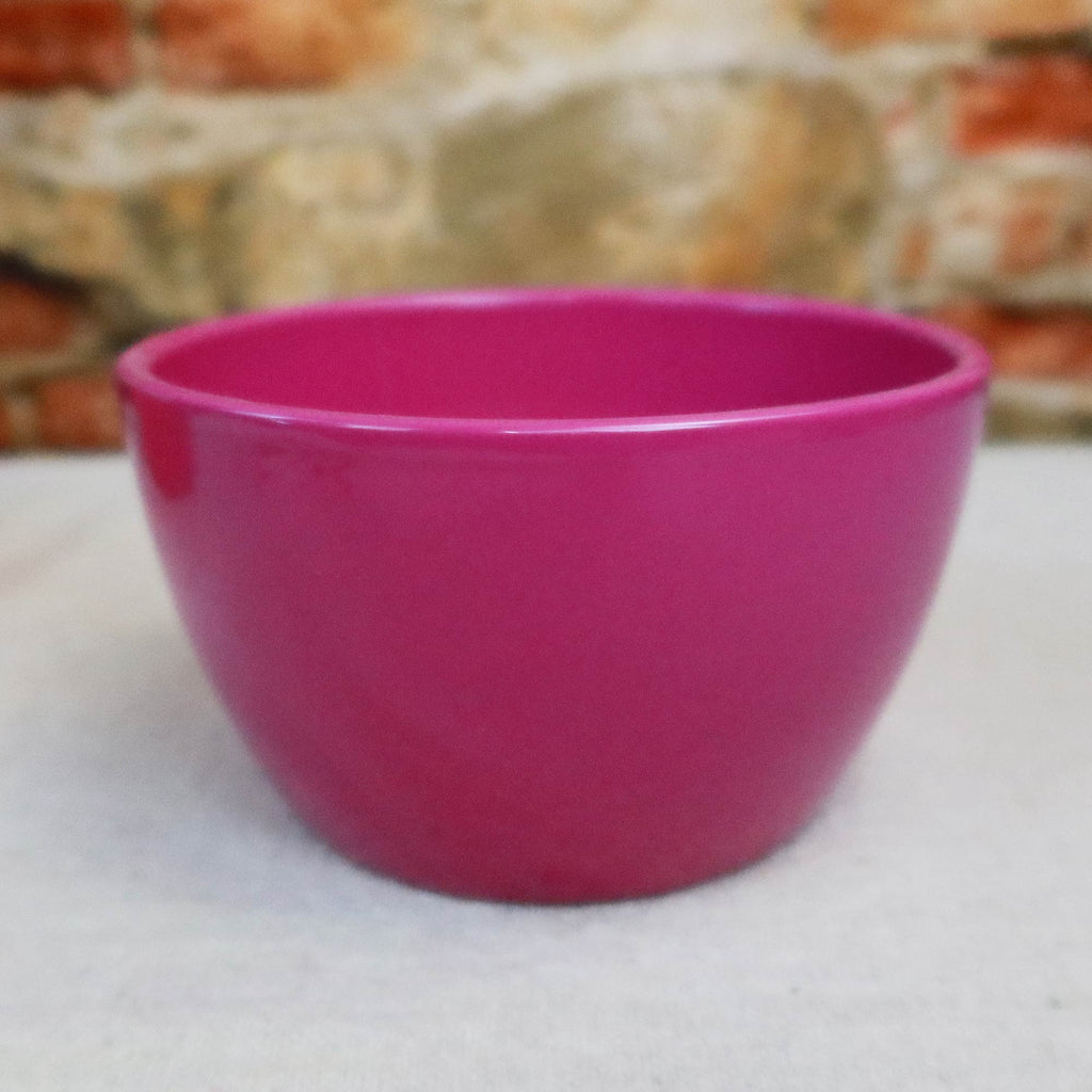 Bright pink Ceramic Garden Bowl displayed on a light surface with a blurred stone and brick wall, suitable as an indoor or outdoor planter.