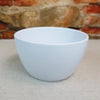 Ceramic Garden Bowl planter in one of nine available colors, displayed on a beige surface with a blurred brick wall background.