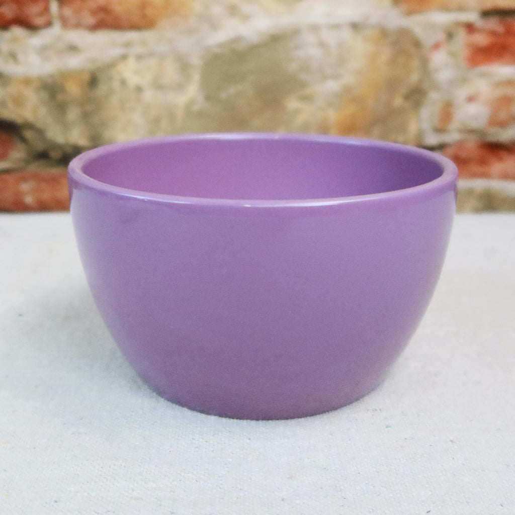 Purple Ceramic Garden Bowl displayed on a light surface, set against a blurred stone and brick wall; suitable for indoor or outdoor plants.