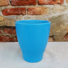 A glossy ceramic pottery planter in a solid color sits on a light surface, with a rustic brick wall backdrop, enhancing the decor.
