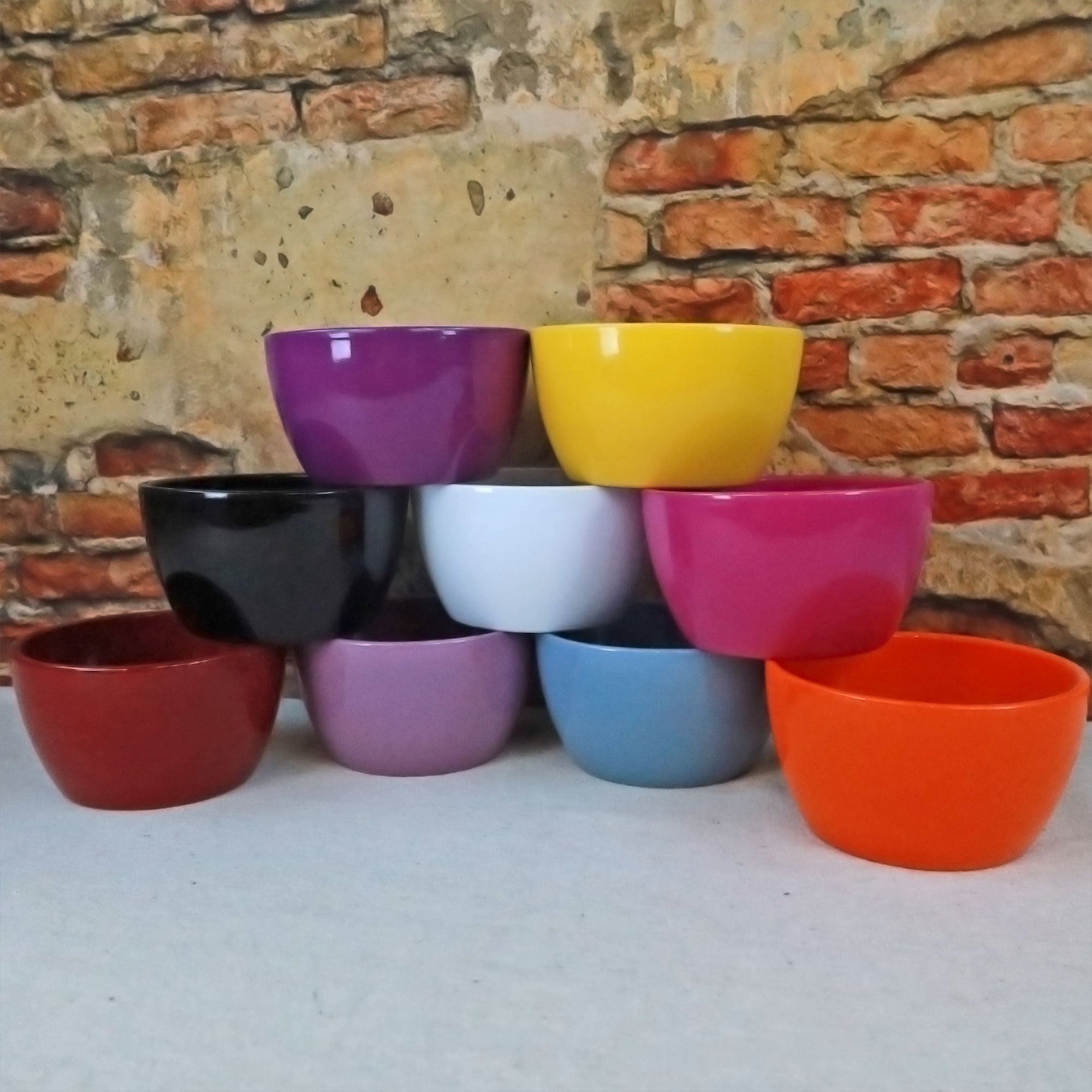 A stack of nine colorful ceramic garden bowls is arranged in a pyramid, perfect as vibrant planters for indoor or outdoor decor.