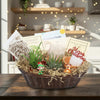 Gift basket with two small potted succulents, care kits, festive figurines, and a Merry Christmas sign on a wooden table.